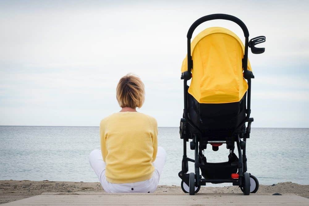 Frau sitzt am Strand mit gelbem Kinderwagen