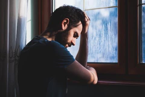 Verzweifelter Mann sitzt traurig an einem Fenster