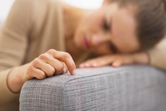 Traurige Frau lehnt mit dem Kopf auf dem Sofa