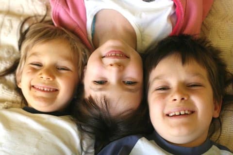 Drei Kinder liegen lachend auf einem Bett 