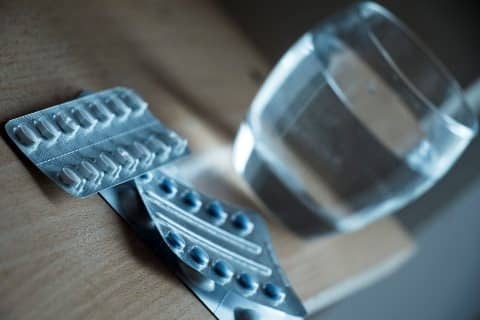 Pillen Verpackung auf einem Holztisch mit einem Wasserglas