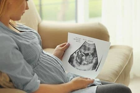 Schwangere Frau sitzt mit Sonogram Bild auf der Couch