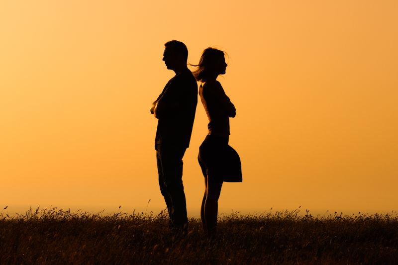 Mann und Frau stehen Rücken an Rücken vor einem Sonnenuntergang