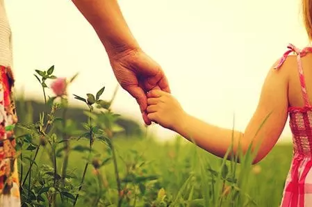 Frau und Kind halten sich an der Hand auf einer Wiese