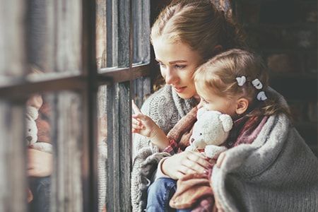 Pflegefamilie Frau hält Kleinkind auf dem Arm und schaut mit ihm aus dem Fenster